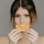A woman holding an orange slice in front of her face